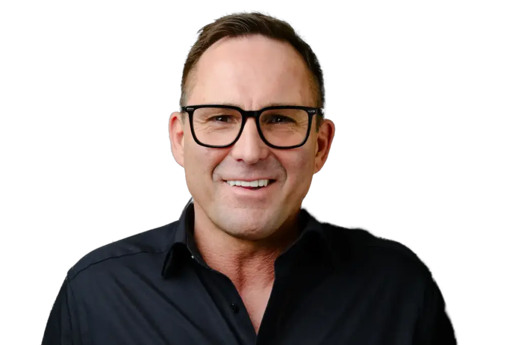 Ein Mann mit kurzen braunen Haaren und Brille lächelt in einem schwarzen Hemd vor einem weißen Hintergrund.