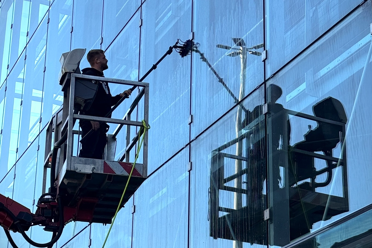 Eine Person reinigt auf einer Hebebühne Fassadenfenster mit einem langen Reinigungswerkzeug.