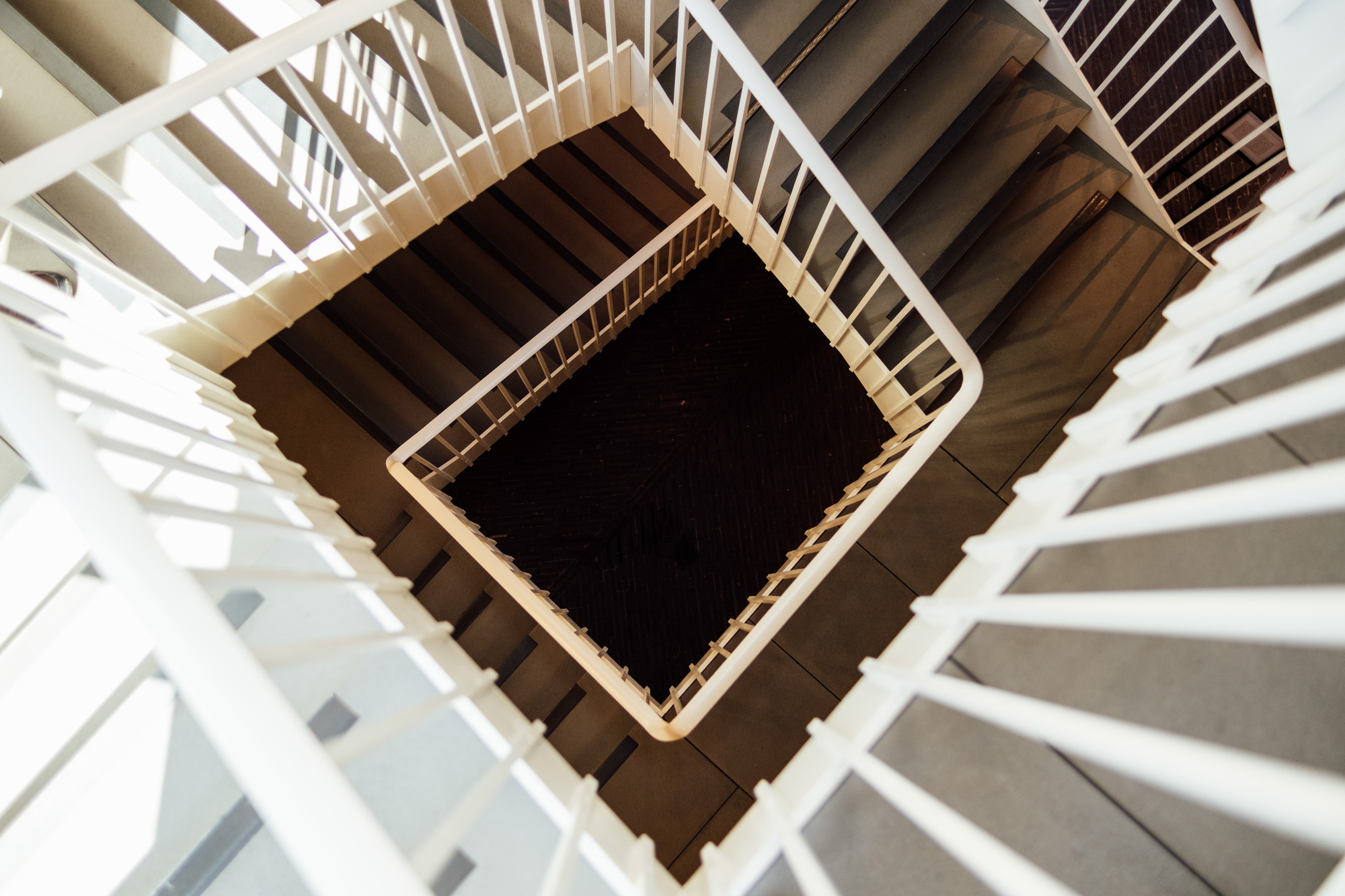 Eine Person reinigt ein quadratisches Treppenhaus mit weißen Geländern; dabei sind geometrische Muster zu erkennen.