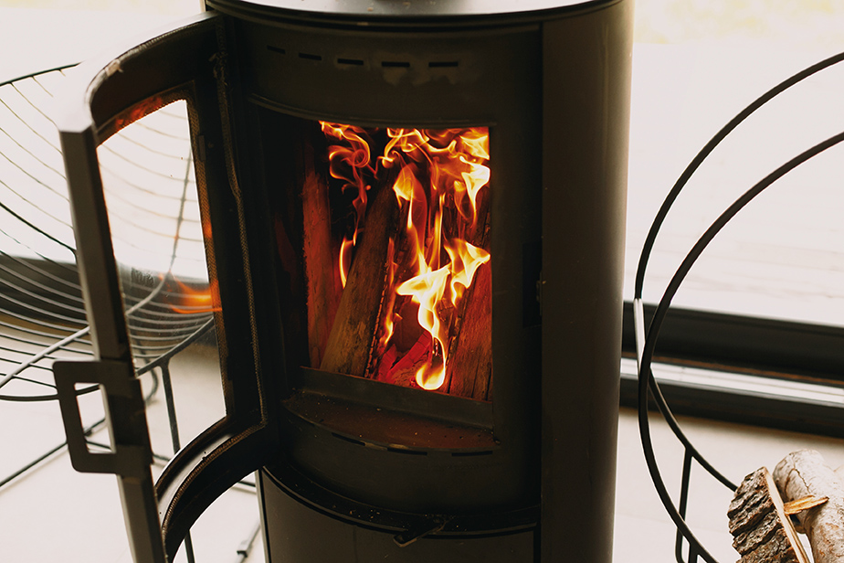 Ein Holzofen steht mit geöffneter Tür; brennende Holzscheite und Flammen sind durch die Glasscheibe zu sehen.