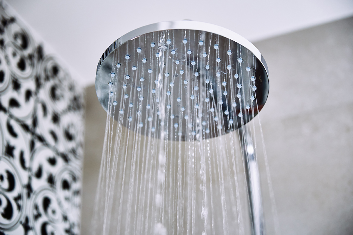 Wasser strömt aus einer modernen, runden Duschbrause in einem gefliesten Badezimmer.